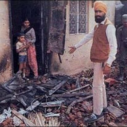 Man in turban standing near burnt debris with a woman in the background.